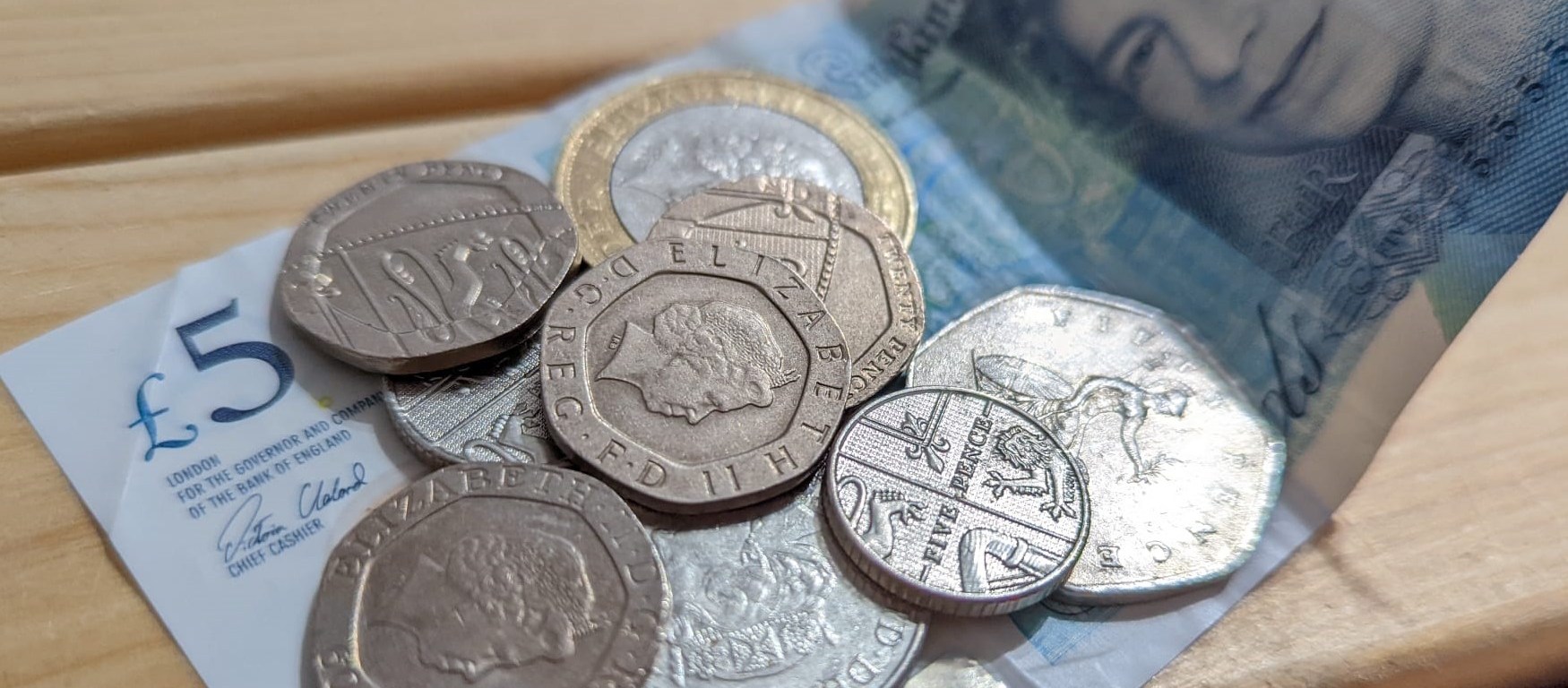 A £5 note, a £2 coin and some silver coins resting on a wooden surface