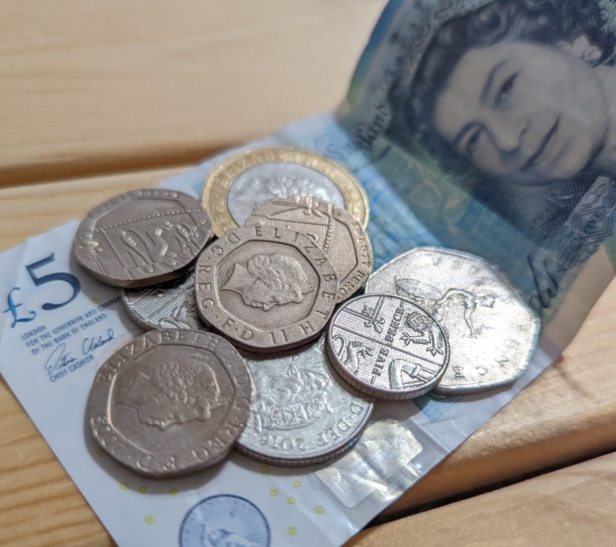 A £5 note, a £2 coin and some silver coins resting on a wooden surface